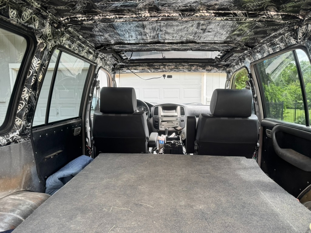 Wide interior view from rear, DynaMat Xtreme throughout ceiling and walls, sleeper deck visible, front seats with checkered Scheelmann fabric