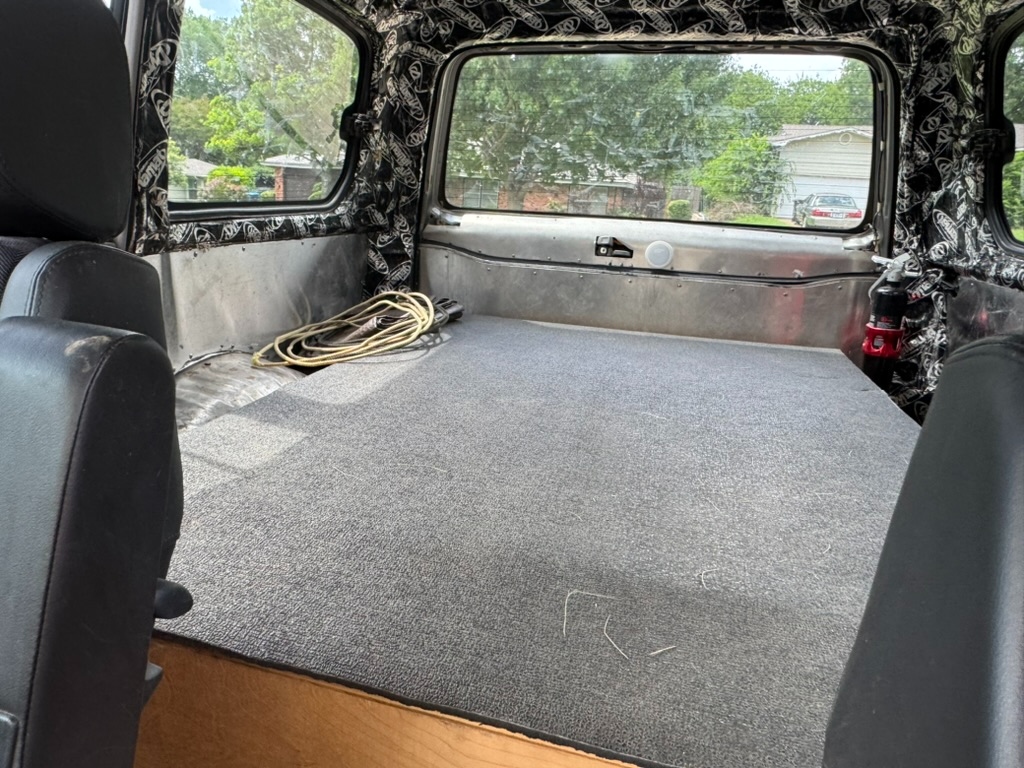 Cargo floor finished with low-pile carpet, DynaMat Xtreme on the headliner, fire extinguisher visible, looking out the rear hatch glass