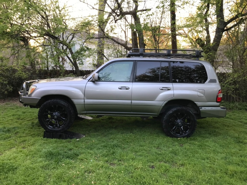 2006 Toyota Land Cruiser 100 Series — Titanium Metallic, ARB bumpers and roof rack, golden hour passenger-side profile on grass