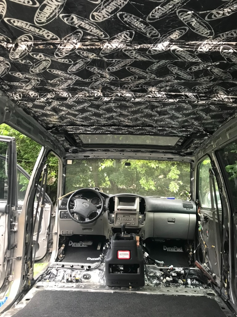 2006 Land Cruiser stripped to bare metal — full Dynamat headliner, DynaPad floors, dash and steering wheel exposed, sunroof open — luxury plastic out, real machine in