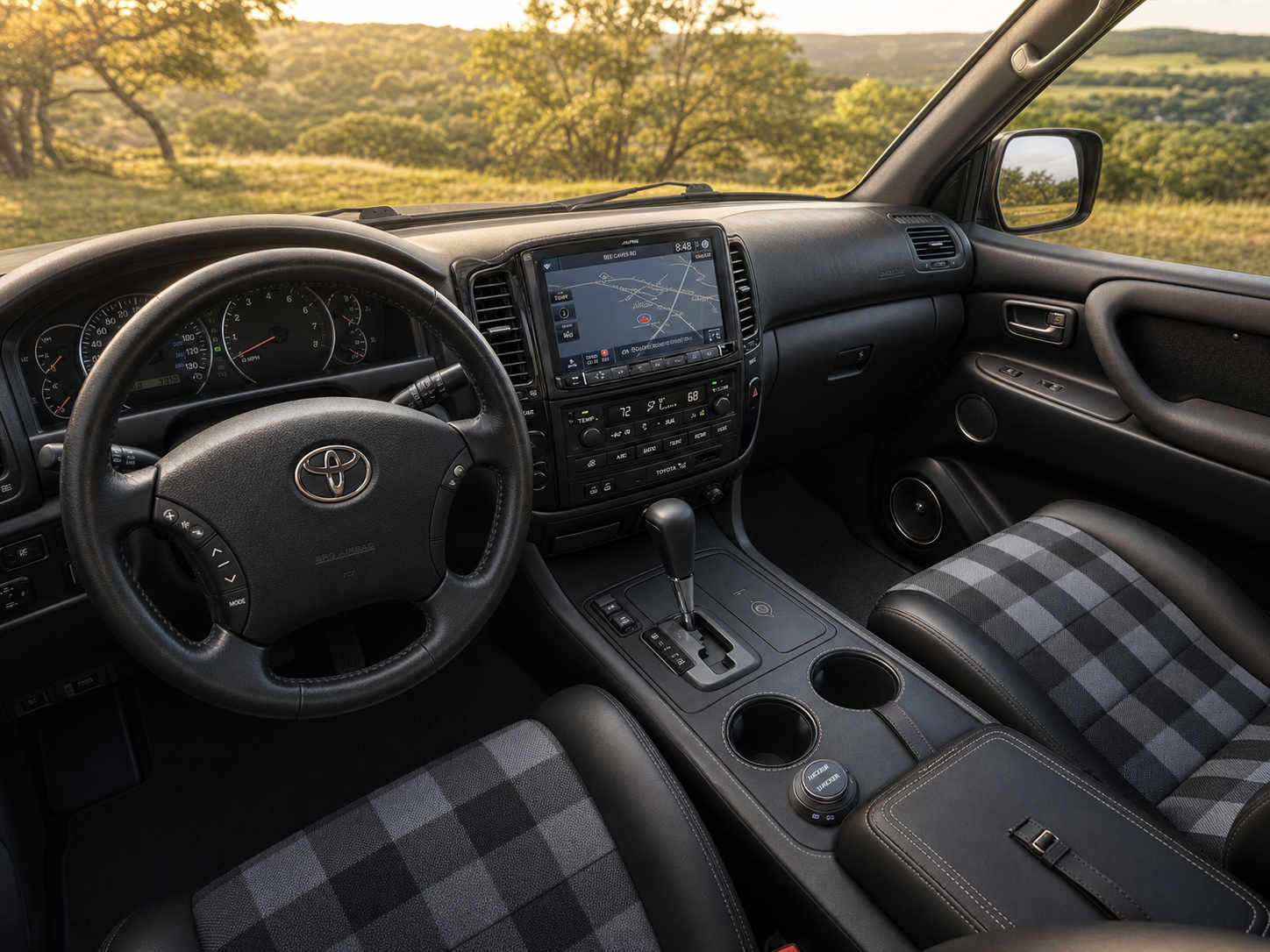 Driver's POV of the finished Land Cruiser interior: Alpine 8-inch LCD, custom black leather center console, Scheelmann seats, Texas Hill Country through the windshield